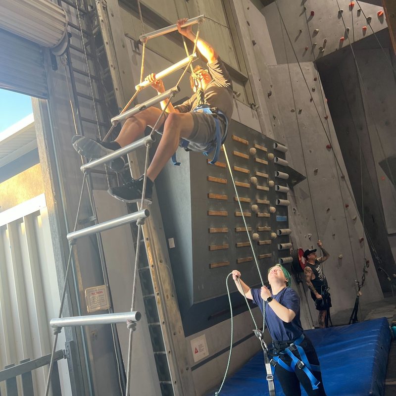 Climbing a rope ladder with a belayer holding the line