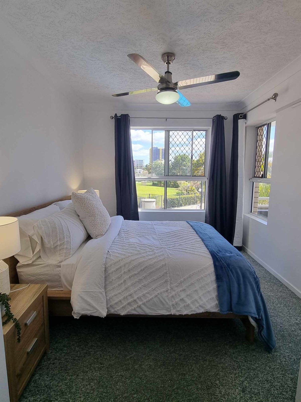 A bedroom with a ceiling fan and a window looking over parkland