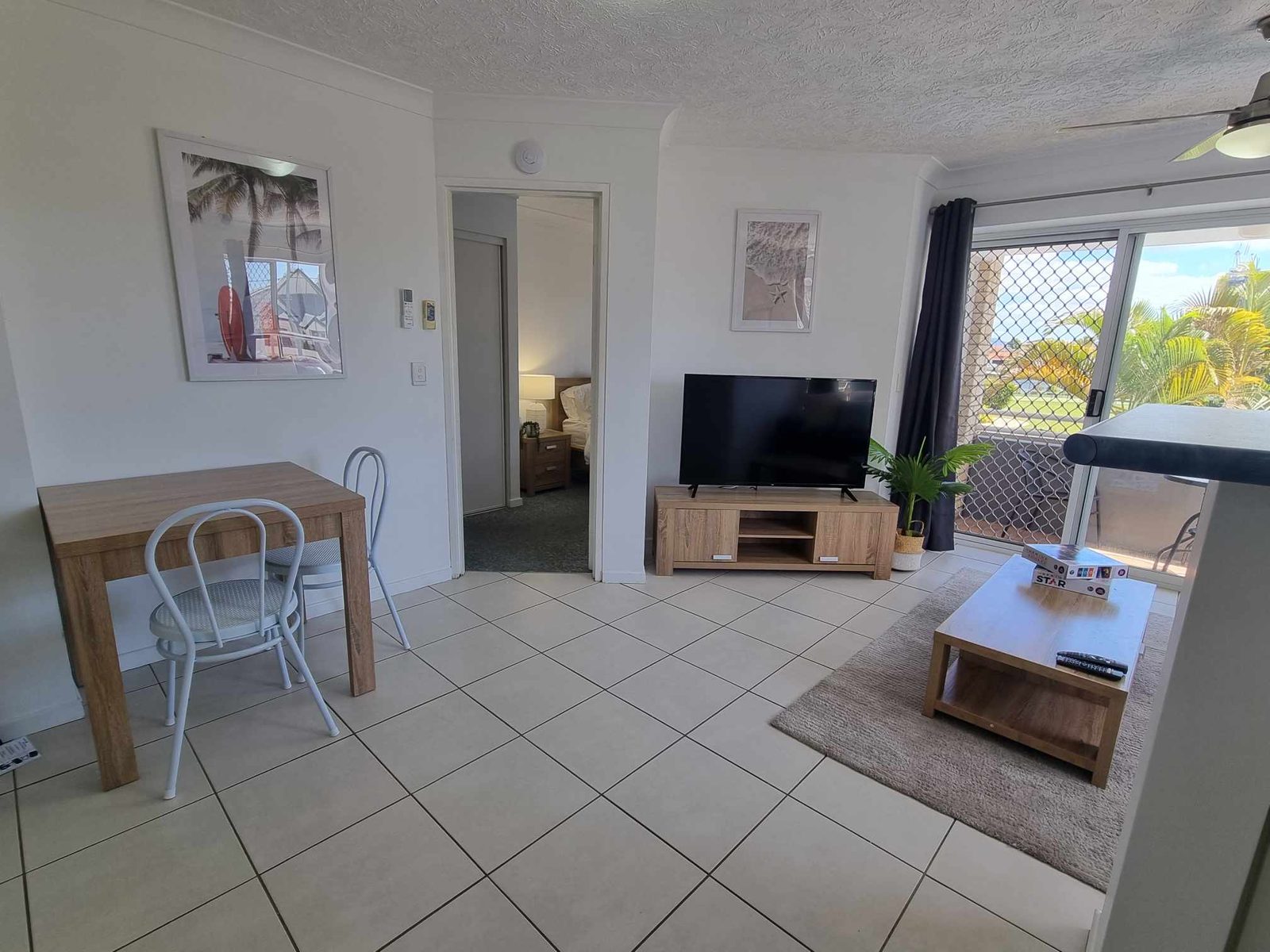 An open-plan living and dining area with a lounge, television and balcony doors