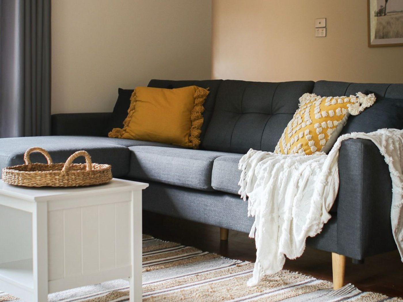 A lounge room with a grey couch, mustard cushions and a white throw